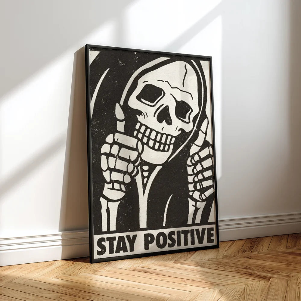 Framed artwork of a skeleton with 'Stay Positive' text. The frame stands on the floor.